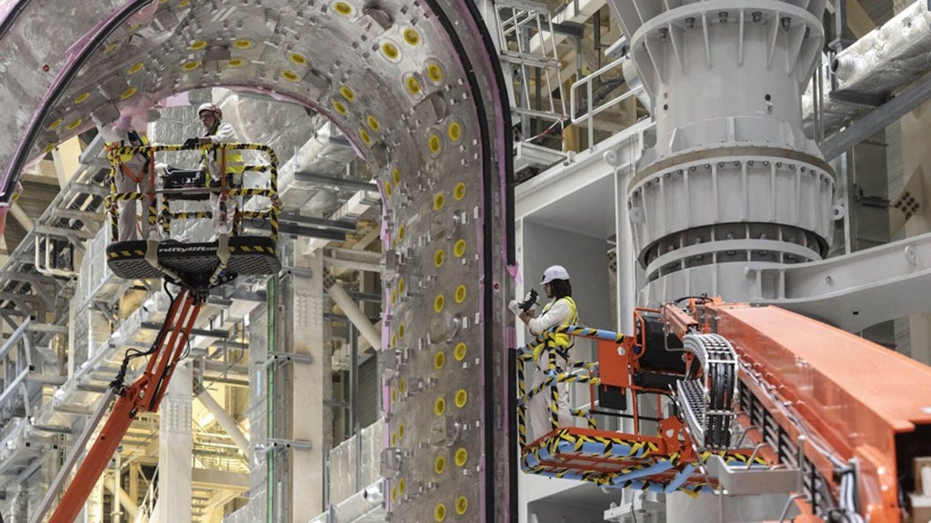 Arbeiter montieren ein grosses metallisches Bauteil in einer modernen Industrieanlage. Die Szene zeigt präzise Ingenieurarbeit auf der Baustelle eines technologischen Grossprojekts.