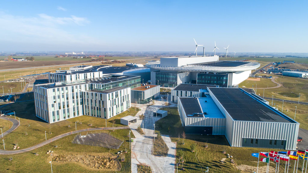 Aerial view of a modern research and operations facility with multiple buildings, green areas, and flags in the foreground.