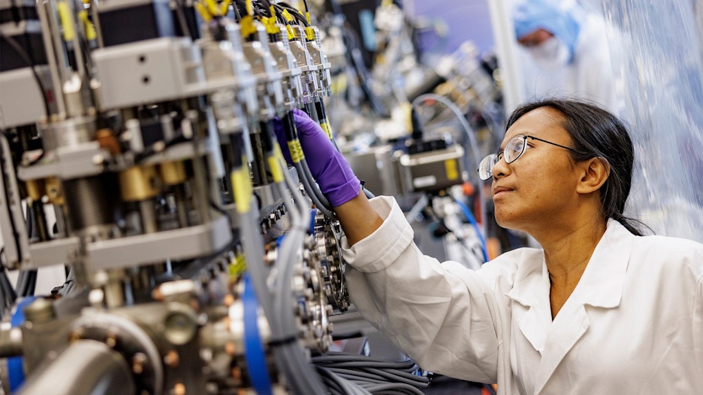 Person in protective clothing working on a complex technical setup with metal components.
