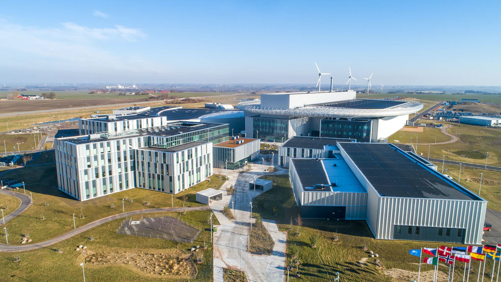 Vue aérienne d’un complexe moderne composé de plusieurs bâtiments entourés d’espaces verts et de drapeaux au premier plan.