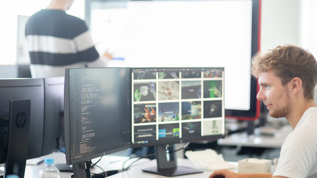 Persona che lavora al computer con due monitor che mostrano codice e una galleria di immagini.