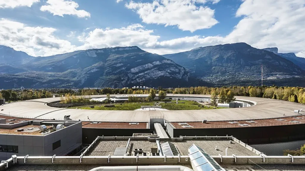 Struttura di ricerca circolare con edifici in primo piano e montagne sullo sfondo.